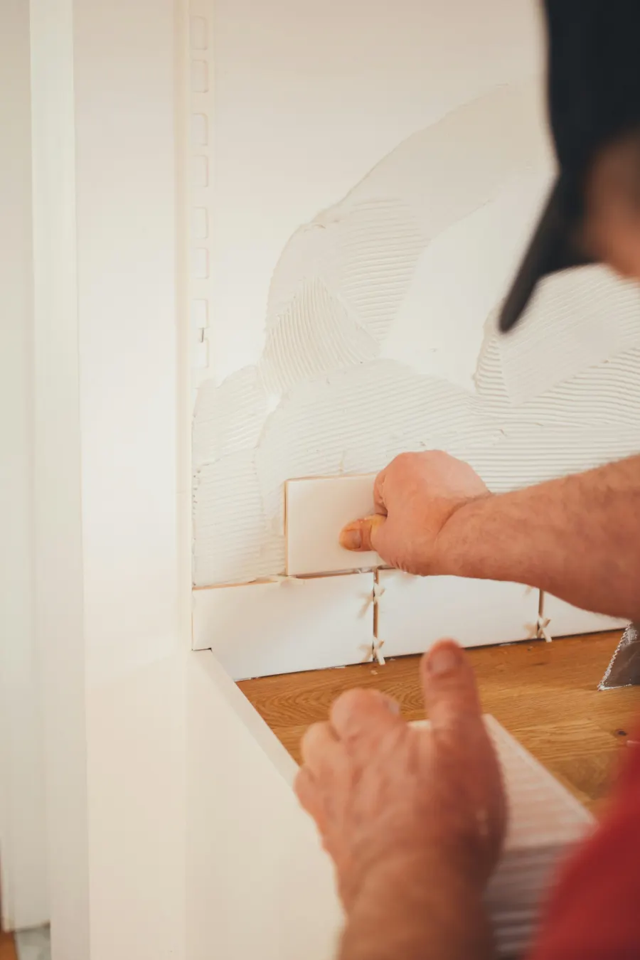 Mãos de um profissional assentando azulejo branco com espaçadores em uma parede