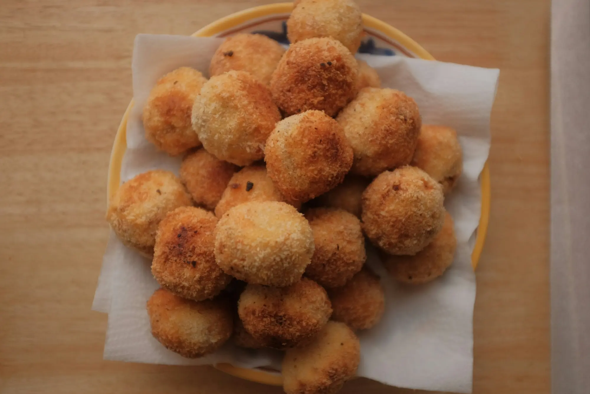 Prato de salgados redondos recém-fritos e dourados, sobre papel toalha, visto de cima