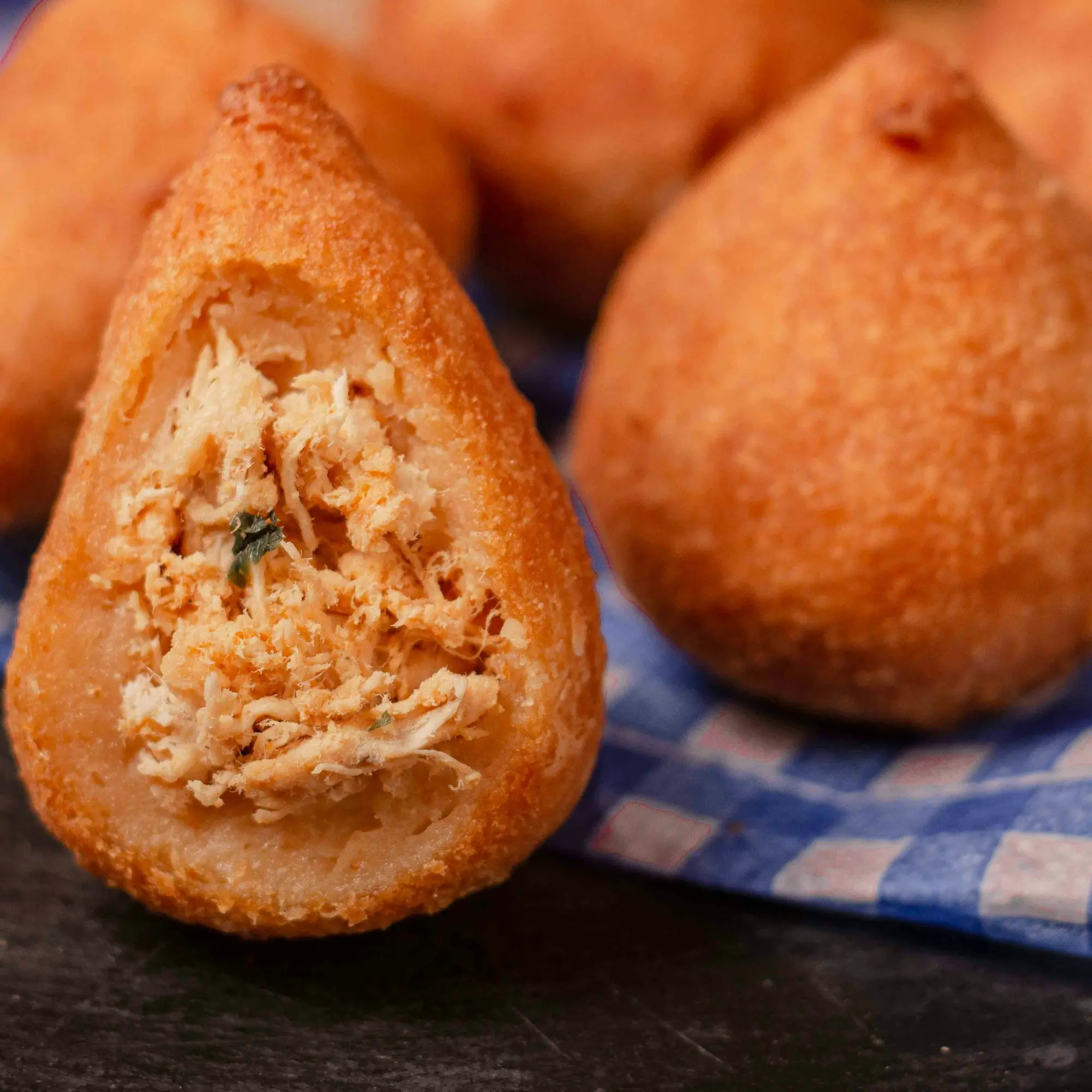 Coxinha partida ao meio, com o frango desfiado à mostra, na frente de outras inteiras