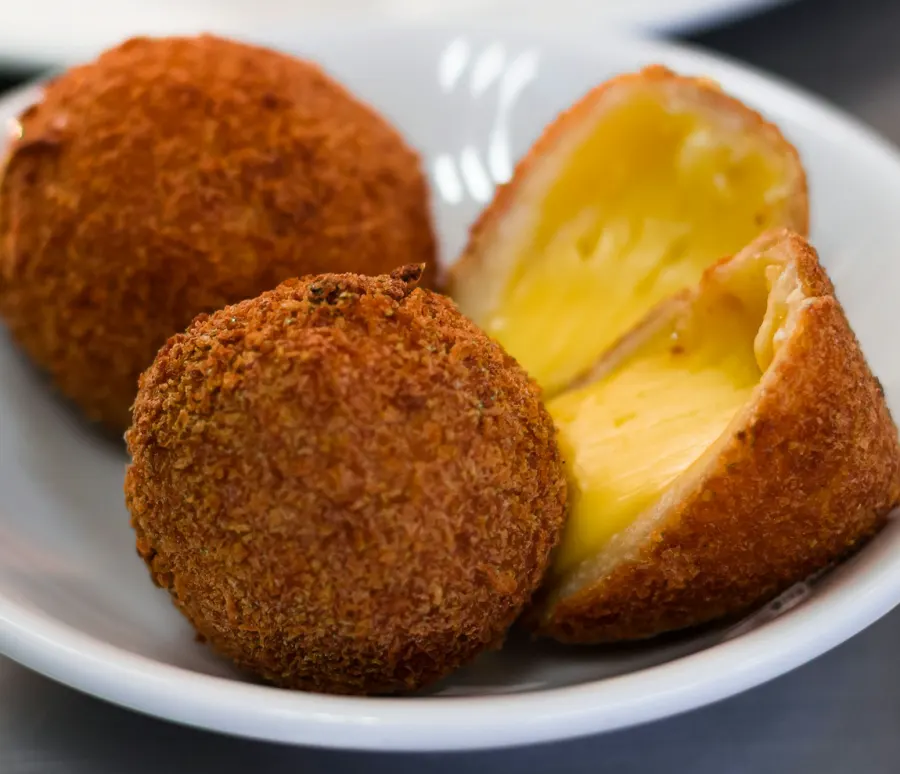 Bolinhas de queijo empanadas numa tigela branca, uma partida ao meio com o queijo derretido