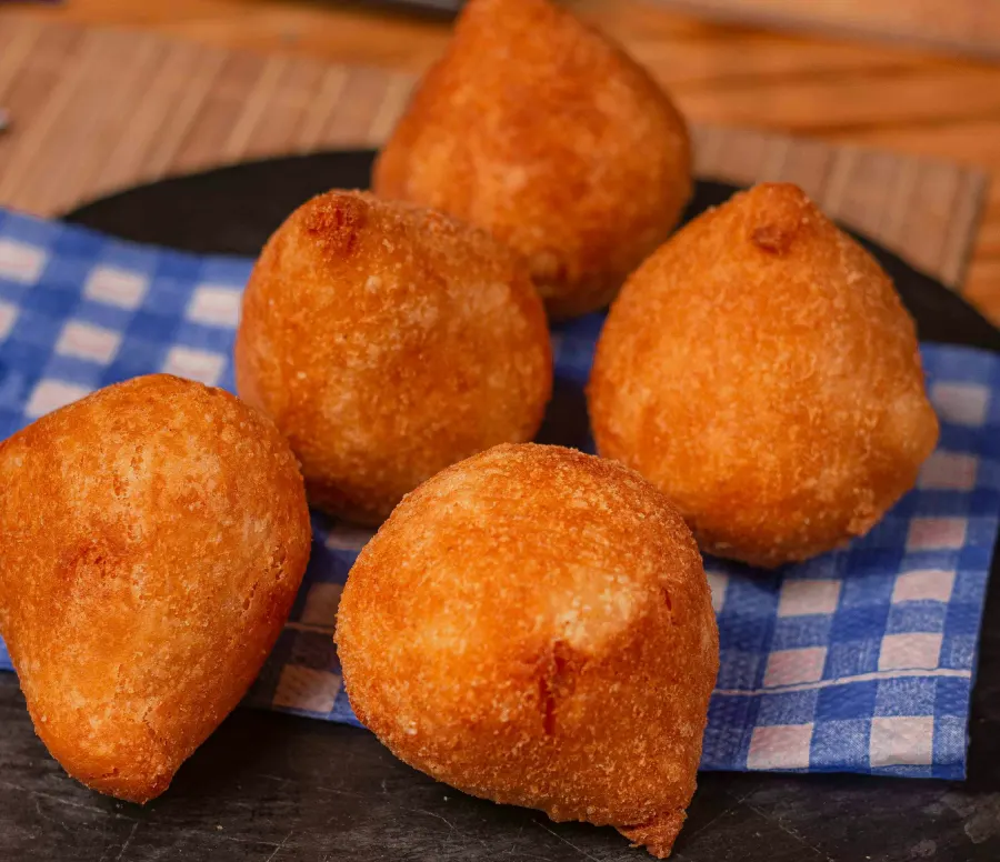 Cinco coxinhas de frango douradas sobre uma pedra escura e um guardanapo xadrez azul