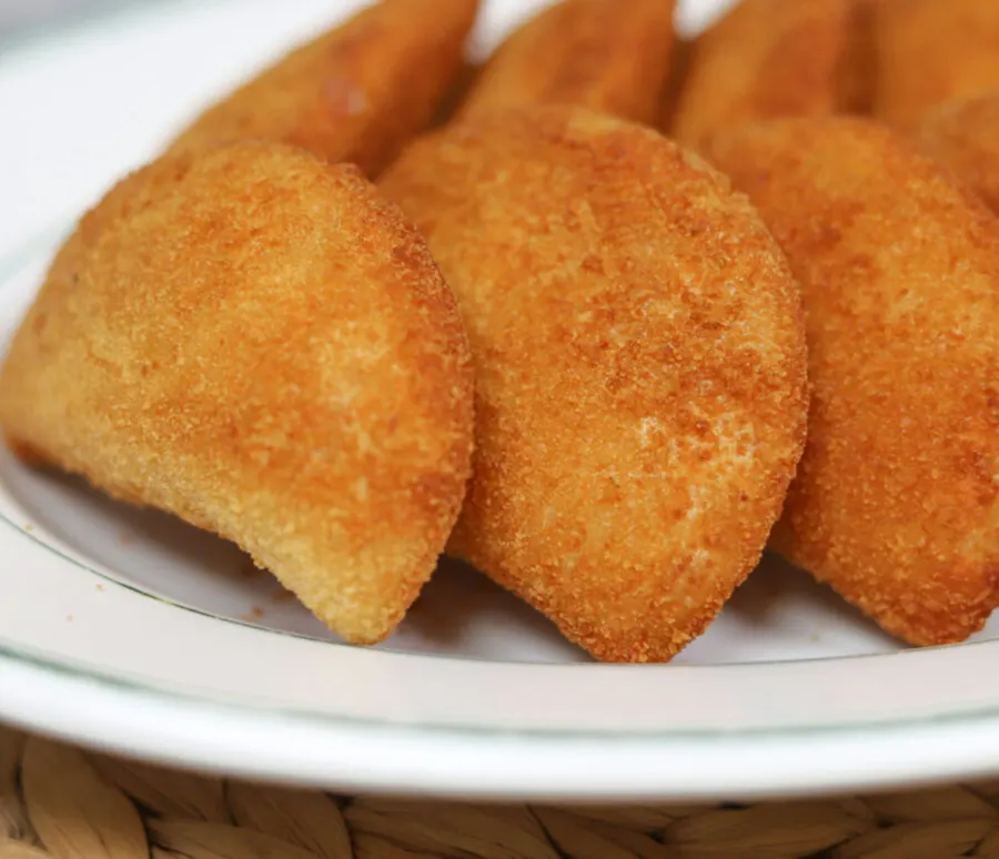 Risoles de carne de sol empanados e dourados, em meia-lua, encostados num prato branco