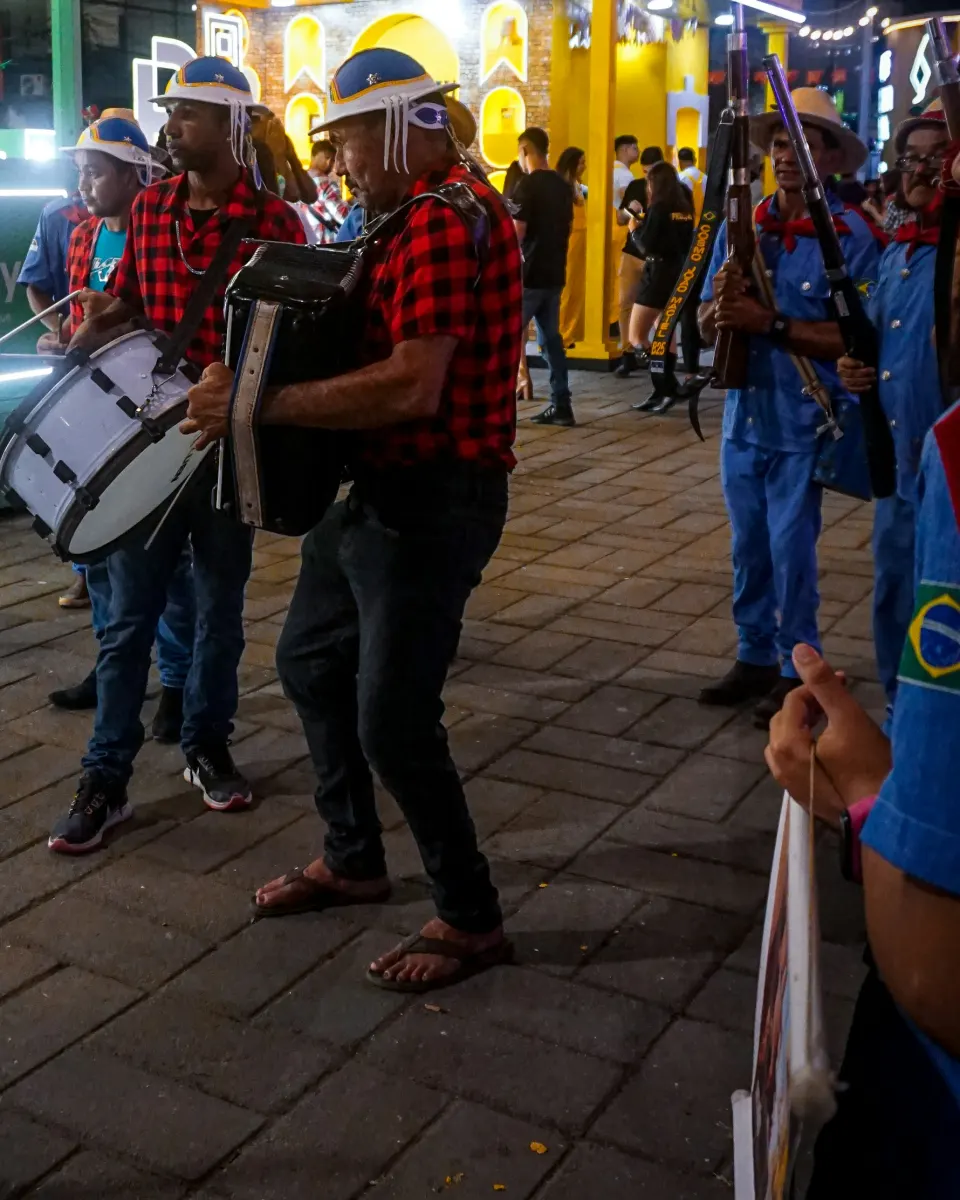 Músicos de bandana e chapéu tocando sanfona, zabumba e pífano numa rua de noite