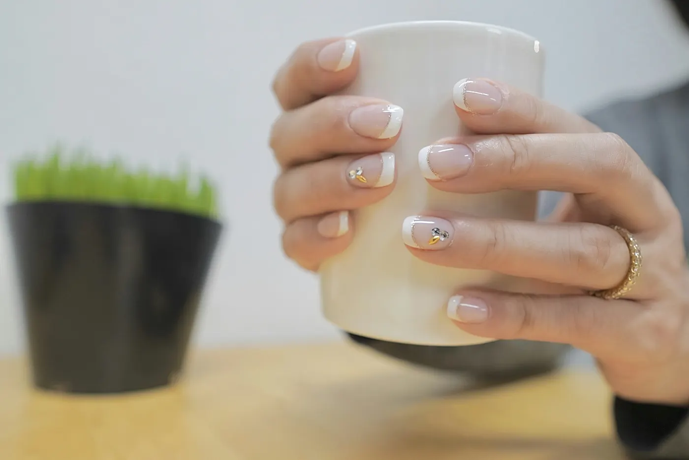 Mãos segurando uma caneca branca, com unhas em francesinha