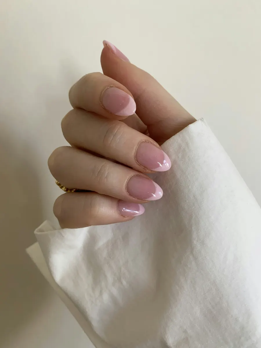 Mão com unhas em rosa translúcido brilhante sobre um tecido branco