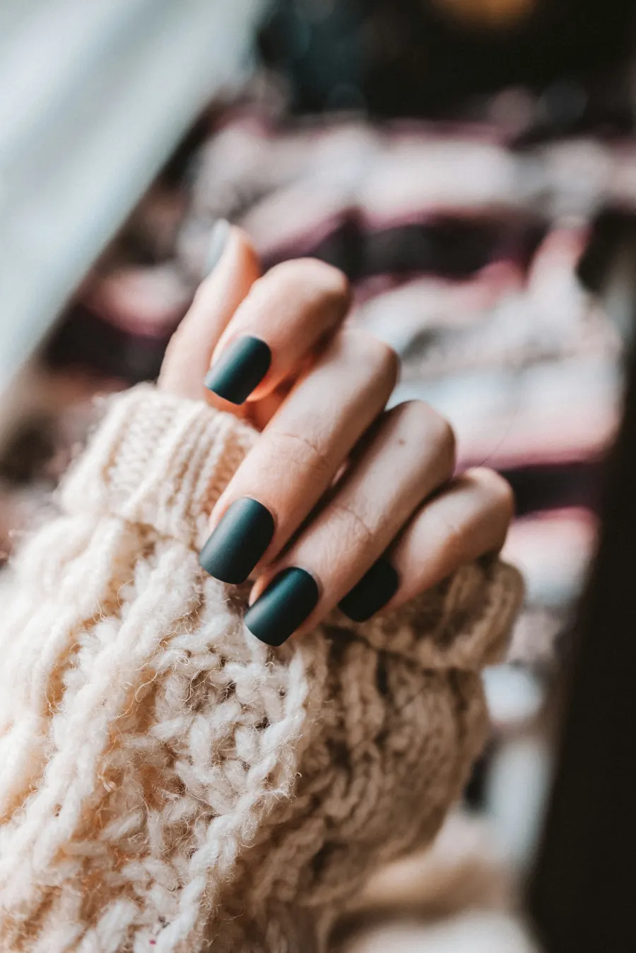 Mão com unhas quadradas em verde escuro fosco, com a manga de um tricô claro